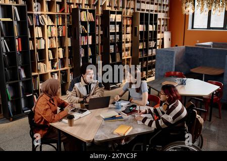 High angle view of four young ethnically diverse gen Z students sitting at table in modern university library preparing for tests Stock Photo
