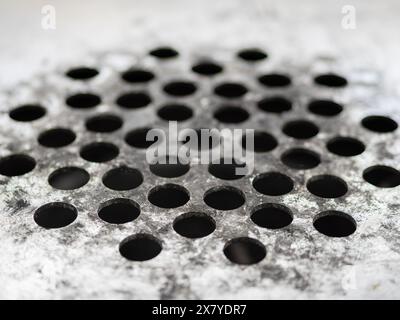 An aged ashtray metallic surface with grid-like patterns of circular holes Stock Photo