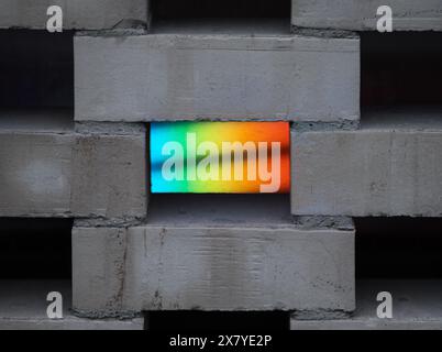 A close-up of grey concrete bricks with a rainbow light gap, creating vibrant colors against the neutral backdrop. Stock Photo