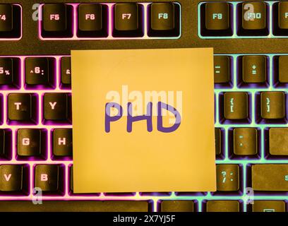 Doctorate of Philosophy concept. PHD written on a yellow sticker lying on the keyboard with a colored backlight Stock Photo