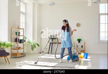 Cheerful happy cleaner, female homeowner having fun while tidying up at home vacuuming carpet, floor Stock Photo