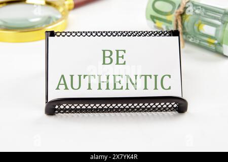 Text Be Authentic on a white card on a white background in a composition with EURO bills and a magnifying glass Stock Photo
