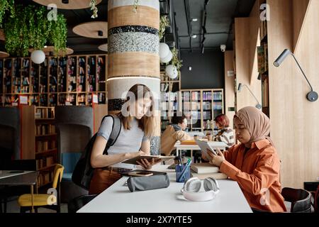 Ethnically diverse female students sitting in front of each other at table in university library preparing for exam or test Stock Photo