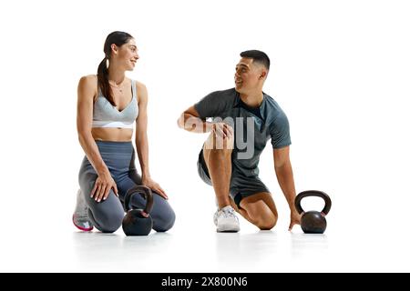 Portrait of man and woman taking break from their workout, kneeling on floor and smiling at each other against white studio background. Stock Photo