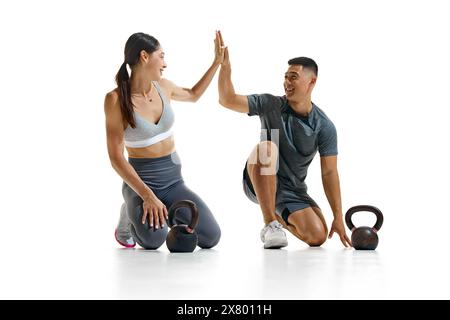 Portrait of man and woman taking break from their workout, kneeling on floor and give high five against white studio background. Stock Photo