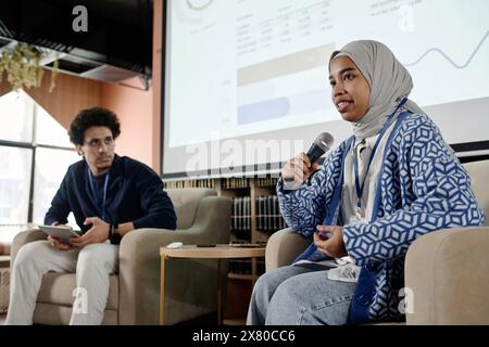 Low angle of young female student wearing hijab sitting in armchair speaking at conference in modern college Stock Photo