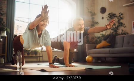 Happy Middle Aged Couple Doing Gymnastics and Yoga Stretching Exercises Together at Home on Sunny Morning. Senior Man and Woman Motivate Each Other to be Healty. Lifestyle and Fitness. Stock Photo