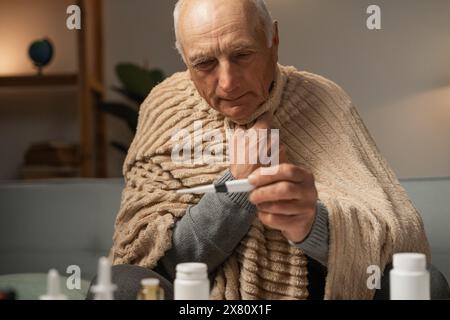 Close-up of man in blanket, holding thermometer with one hand. Treatment for coronavirus. Stock Photo