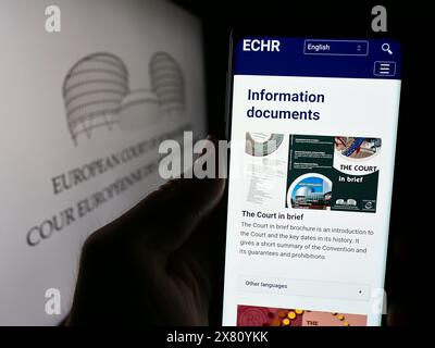 Person holding cellphone with webpage of international court European Court of Human Rights (ECHR) with logo. Focus on center of phone display. Stock Photo