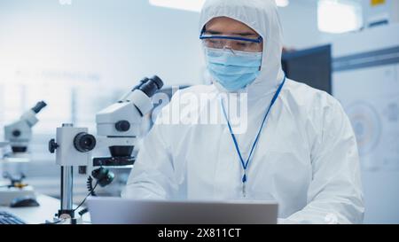 Modern Technology Concept: Engineer in Coverall Working on Laptop Computer. Electronic Manufacturing Factory Technician Testing New Electrical Equipment and Inserting Analytic Science Data. Stock Photo