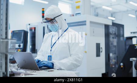 Modern Technology Concept: Engineer in Coverall Working on Laptop Computer, Examining a Circuit Board with Microchips and Typing Data. Technician Testing New Electrical Equipment. Stock Photo