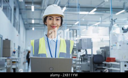 Portrait of a Happy and Smiling Asian Female Engineer in White Hard Hat Standing with Laptop Computer at Electronic Manufacturing Factory. Successful Employee Posing for Camera. Stock Photo