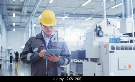 Portrait of a Young Asian Man, Working as an Engineer at a Factory Facility, Wearing Work Jacket and a Yellow Hard Hat. Heavy Industry Specialist Working on Tablet Computer. Stock Photo