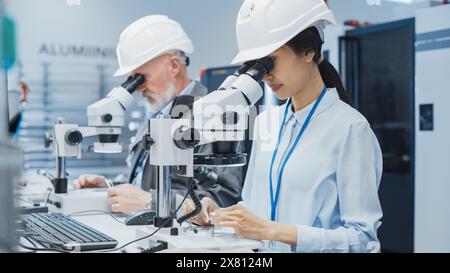 Modern Technology Concept: Two Scientists Examining Small Scale Industrial Equipment Parts Through a Microscope. Technicians Testing New Factory Components for Quality. Stock Photo