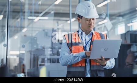 Research and Development Specialist Using Laptop to Operate a Heavy Industry Machine at a Factory. Asian Male Technician Configuring Industrial Machinery with the Help of Computer. Stock Photo