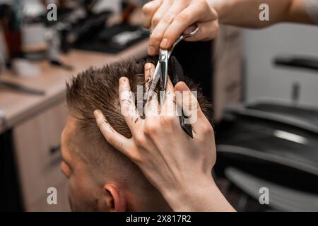 Professional barber styling hair of his client in the barbershop using scissors and comb. Stock Photo