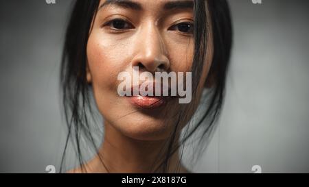Close Up of the Face of a Strong Asian Female Looking at Camera and Smiling. Proud Woman Fighting Against her Fears and Winning Against Injustice, Prejudice, Mental Illness Stock Photo
