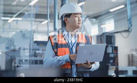 Portrait of an Asian Male Engineer in Orange Safety Vest Working on Laptop Computer at Electronic Manufacturing Factory. Technician Working on Daily Tasks and Research and Development Data. Stock Photo