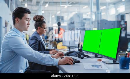 Factory Office Room: Industrial Engineers Developing Models of a Heavy Industry Machine Parts on a Computer 3D Software. Two Computer Monitor Displays are a Green Screen Mock Up Template. Stock Photo