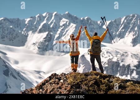 Two happy active hikers are standing in winner pose with open arms against glacier and mountain Stock Photo