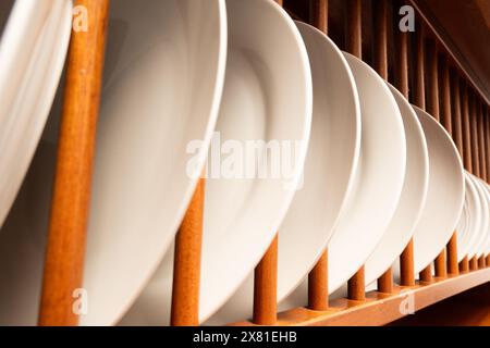 A wooden rack with many white plates on it. The plates are stacked in a neat and orderly fashion Stock Photo