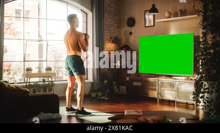 Home Training: Handsome Muscular Black Man Using Kettlebell, Exercising with Trainer via TV Online Video App. Strong Mixed Race Sportsman Using Chroma Key Green Screen for Virtual Gym. Stock Photo