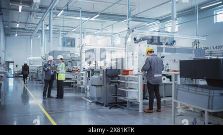 Industrial Factory: Team of Engineers, Technicians and Workers, Working on Production Plant, Developing CNC Parts, Programming Machines. Two Specialists Discussing Project Plan and Using Laptop. Stock Photo
