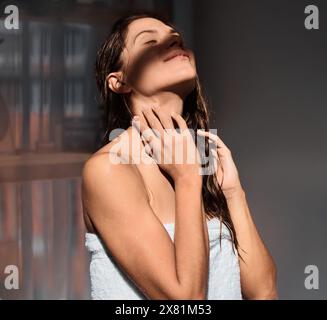 Woman, towel and relax in morning sun after shower in home bedroom or skin care, dermatology or beauty. Female person, calm and peaceful at window or Stock Photo