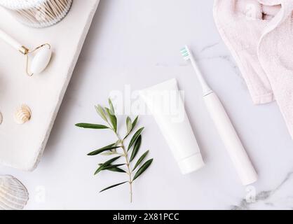 Top view of white plastic tube without label, electric toothbrush and olive branch on white bath background. Mockup scene for cosmetic, toothcare. Cop Stock Photo