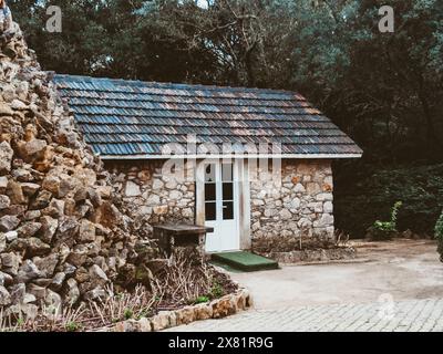 Rustic farmhouse built from natural stone with a small stone wall surrounded by trees Stock Photo