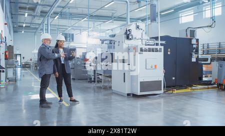 Portrait of Two Heavy Industry Employees in Hard Hats at Factory. Checking and Discussing Industrial Facility, Using Tablet Computer. African American Engineer and Middle Aged Technician at Work. Stock Photo