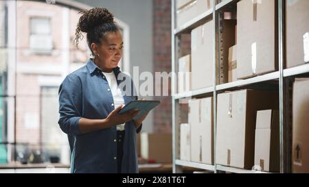 Portrait of a Successful Employee Checking Inventory, Writing in Tablet Computer. Black Woman Posing for Camera and Smiling in a Warehouse Storeroom with Orders Ready for Shipment. Stock Photo