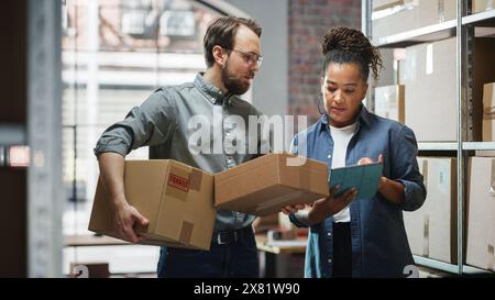 Female Inventory Manager Using Tablet Computer, Talking to a Worker Holding Two Cardboard Packages. They Discuss Customer Orders. Stock of Parcels with Products Ready for Shipment in the Background. Stock Photo