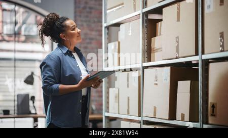 Portrait of a Manager Checking Inventory, Writing in Tablet Computer. Black Woman Working in a Warehouse Storeroom with Rows of Shelves Full of Parcels, Packages with Orders Ready for Shipment. Stock Photo
