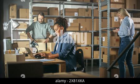 Establishing Shot of Multicultural Team of Warehouse Workers at Work in Internet Shop's Storeroom. Small Business Owners and Inventory Managers Working on Laptop, Tablet, Packing Parcels for Delivery. Stock Photo