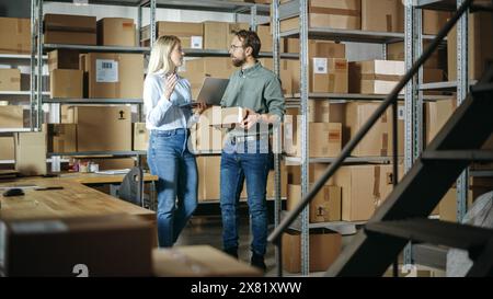 Warehouse Inventory Manager and Worker Walking and Using Laptop Computer, Talking About Parcel Shipment. Small Business Owners Working in Storeroom, Preparing Online Orders for Clients. Stock Photo