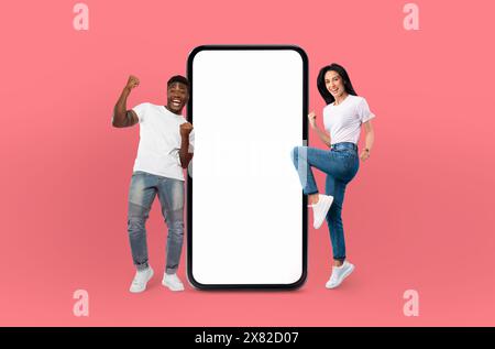 Smiling multiethnic young man and woman stand beside large smartphone Stock Photo