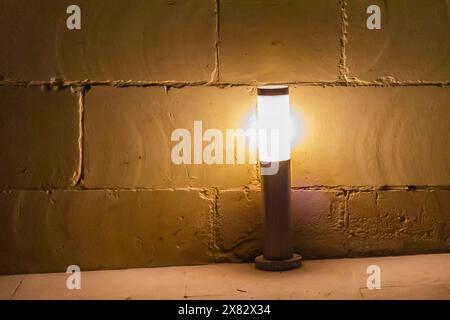 Illuminated yellow light bulb against outdoor wall at night Stock Photo