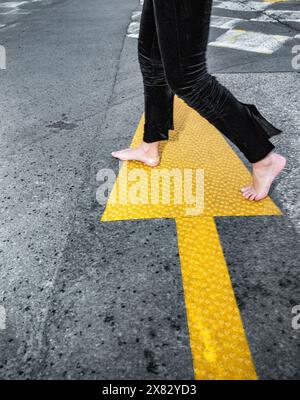 Beautiful black-haired girl on the street, fashion shoot. Wide angle. Barefoot on the asphalt. High-heeled shoes in her hands. Stock Photo