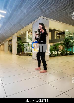 Beautiful black-haired girl on the street, fashion shoot. Wide angle. Barefoot on the asphalt. High-heeled shoes in her hands. Stock Photo