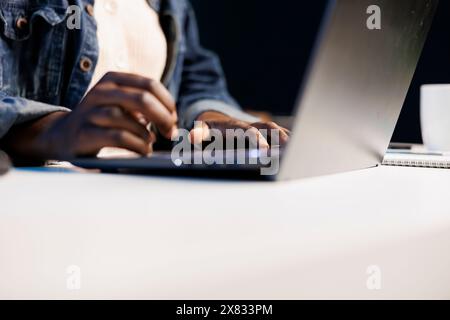 Close up of black person utilizing modern technology by typing on portable computer. Selective focus on hands of african american individual taking notes on laptop and surfing the net. Stock Photo