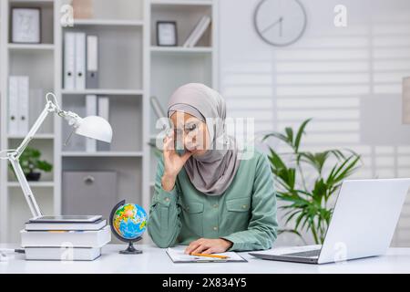 Tired and tired online teacher, woman in hijab working in home office remotely, teaching students and pupils, using laptop at work. Stock Photo