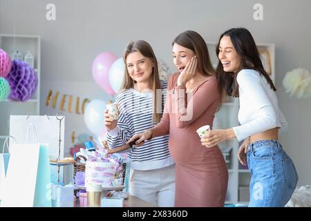 Young pregnant woman with her friends cutting cake at baby shower party Stock Photo