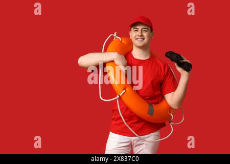 Male lifeguard with ring buoy and binoculars on red background Stock Photo