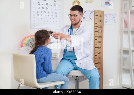 Male pediatric ophthalmologist putting trial frame onto little girl in clinic Stock Photo