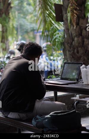 A male student is working on assignments on his laptop in a semi-outdoor room in the afternoon Stock Photo