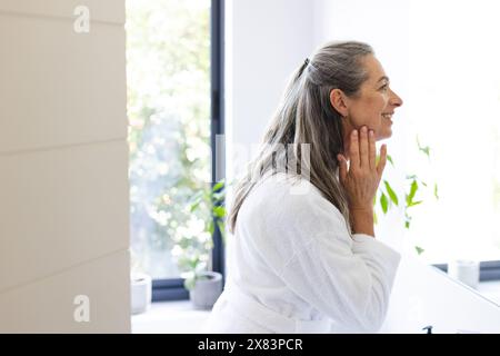 At home, mature Caucasian woman with long gray hair touching her face, copy space Stock Photo