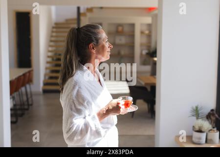 Mature Caucasian woman holding cup of tea, looking out at home Stock Photo