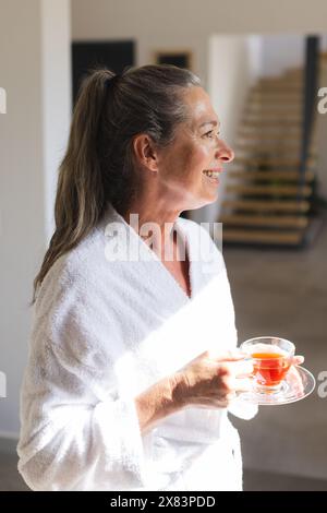 Mature Caucasian woman holding cup of tea, looking away Stock Photo