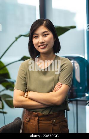 At modern office for business, young Asian woman standing with arms crossed, smiling at camera Stock Photo